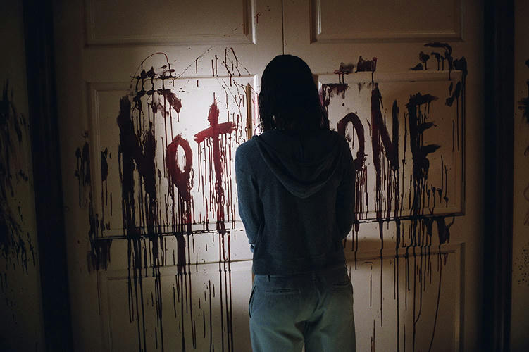 Woman in front of doors with 'Not Alone' written in blood